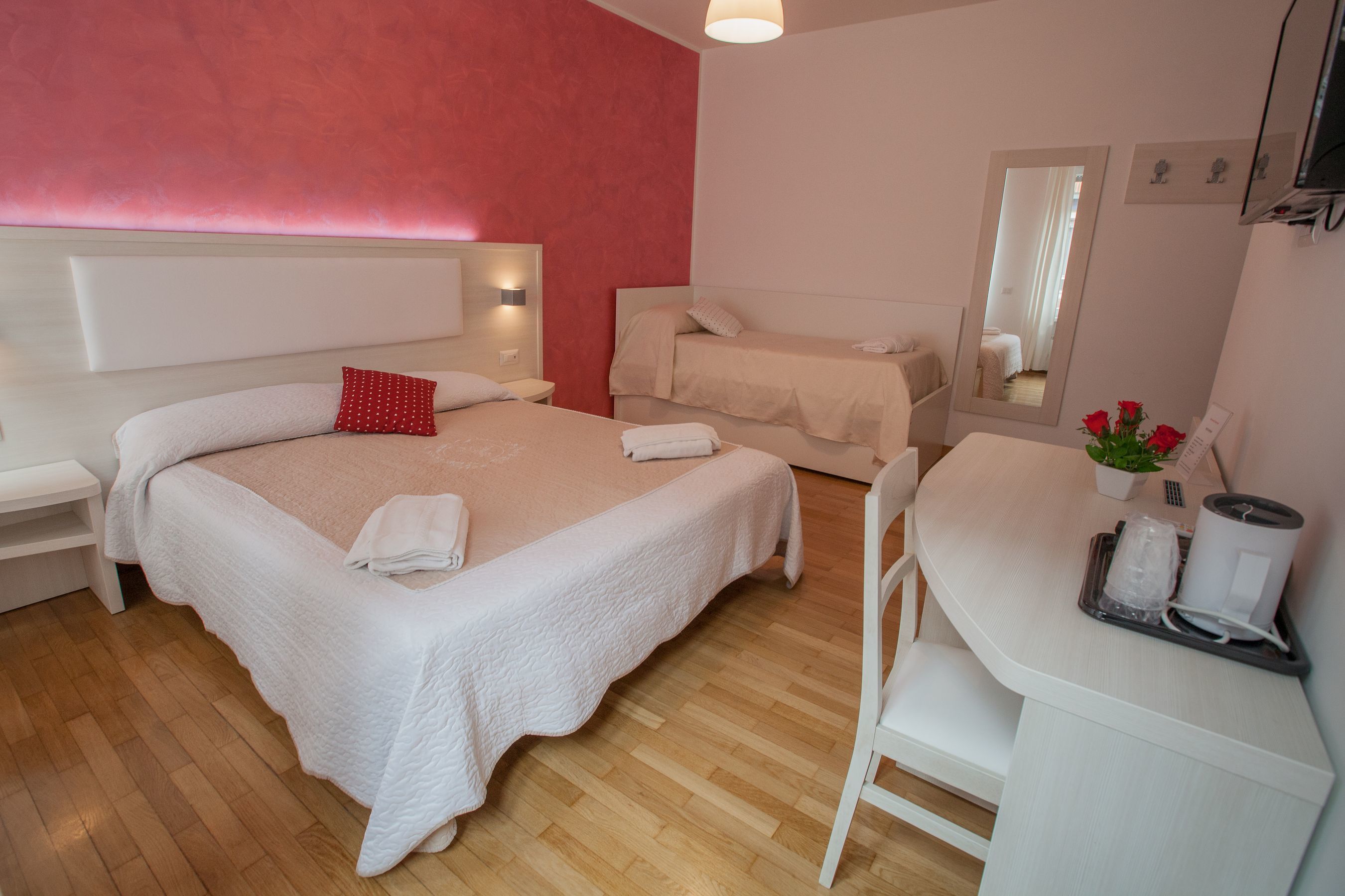 Une chambre d’hôtel avec deux lits, un bureau, une chaise, un miroir et une petite plante.