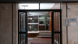 Entrada de hotel com porta de vidro, balcão de recepção e escada que dá acesso ao interior.