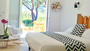 Ein Schlafzimmer mit einem Bett, einem Schreibtisch und einem Stuhl. Ein Fenster bietet Blick auf Bäume und eine Terrasse.