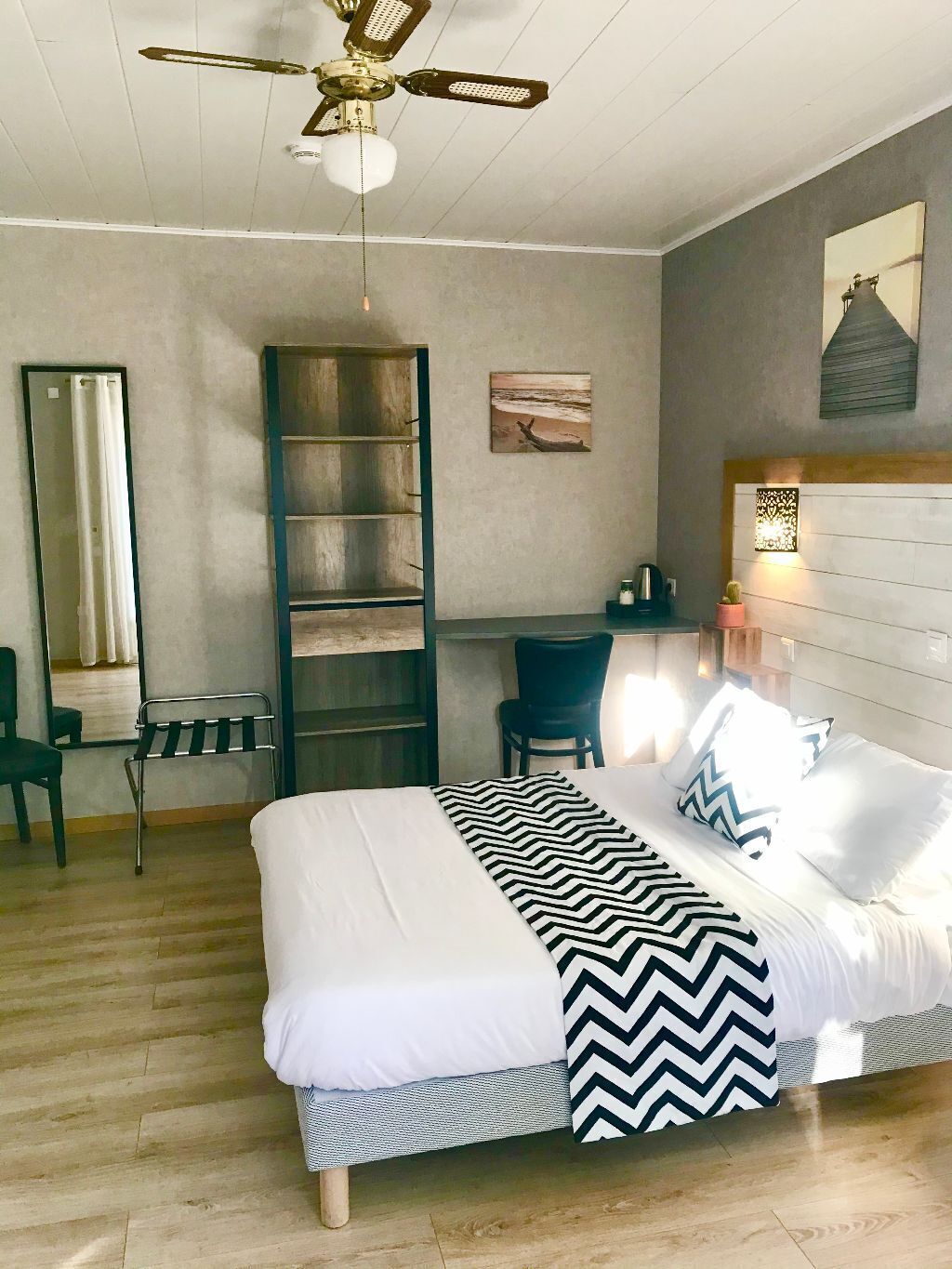 Un dormitorio con cama, escritorio, silla, escalera, espejo y ventilador de techo.
