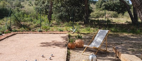 A gravel area with a pool table, two lounge chairs, and a hat on one of the chairs.