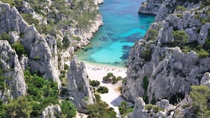Eine Küstenlandschaft mit schroffen Klippen, klarem türkisblauem Wasser und einem Sandstrand.