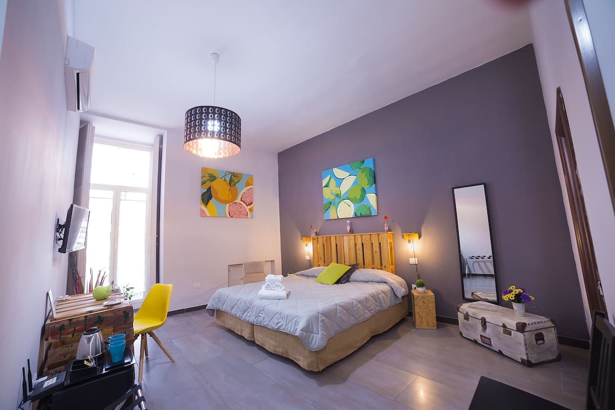 A modern bedroom with a bed, bedside table, chair, and artwork.