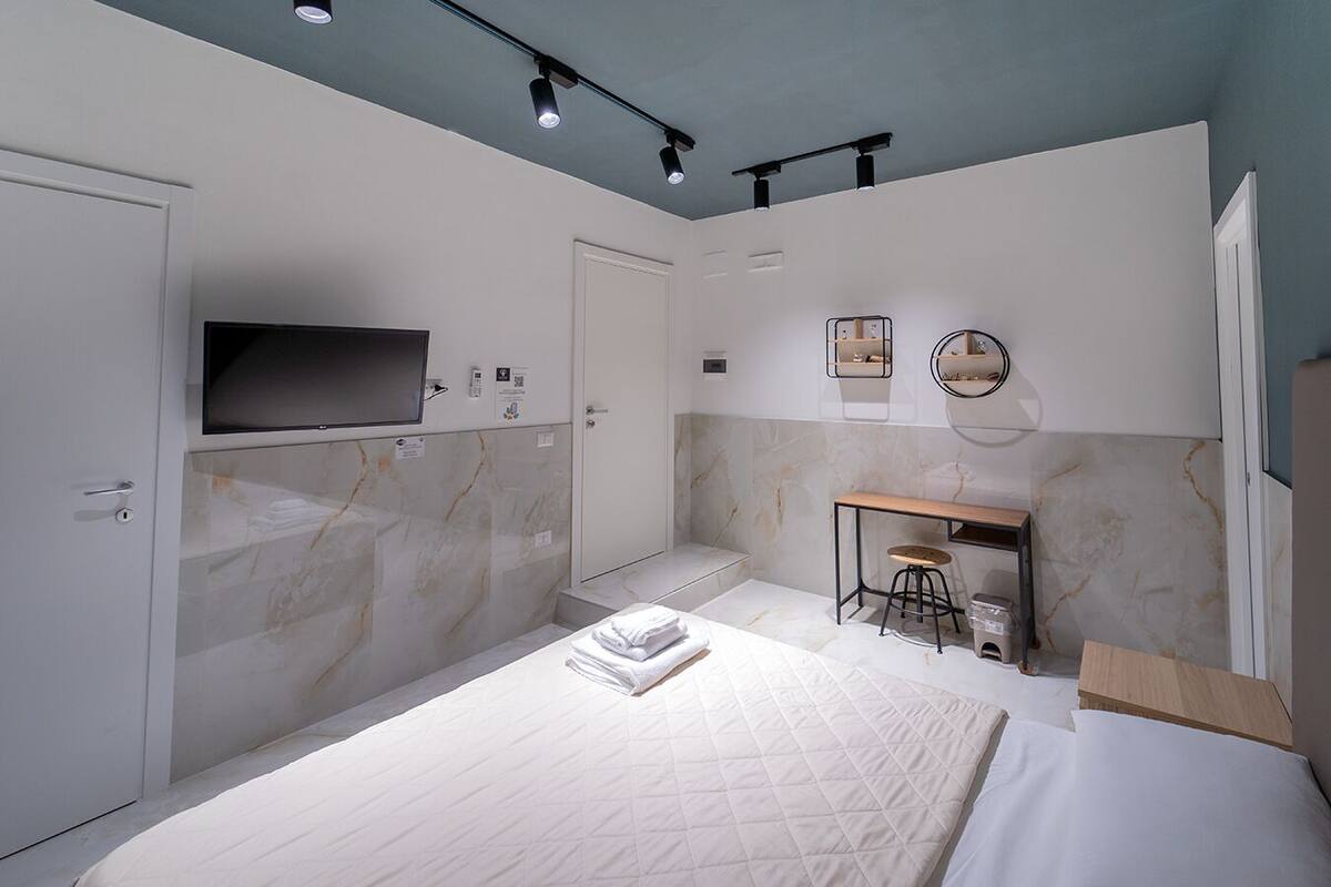 A modern bedroom with a bed, a desk, and a TV mounted on the wall.
