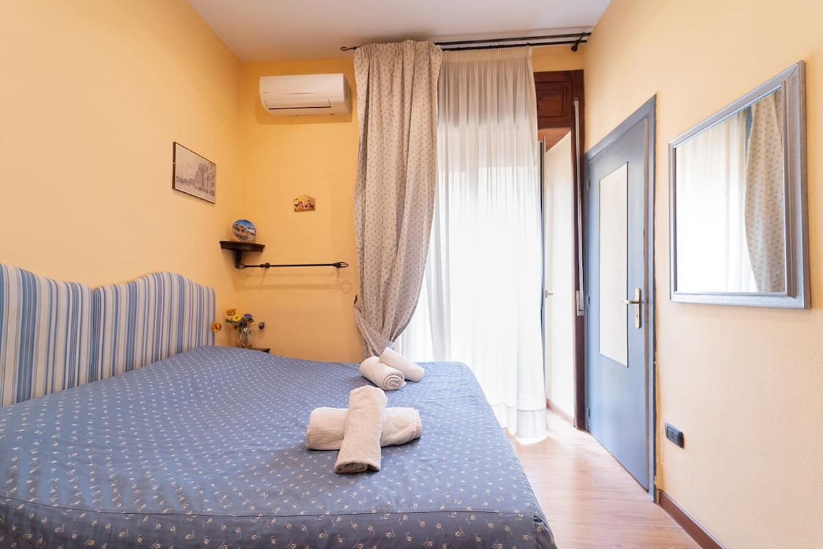 A bedroom with a bed, a window with curtains, a wall-mounted air conditioner, and a door.