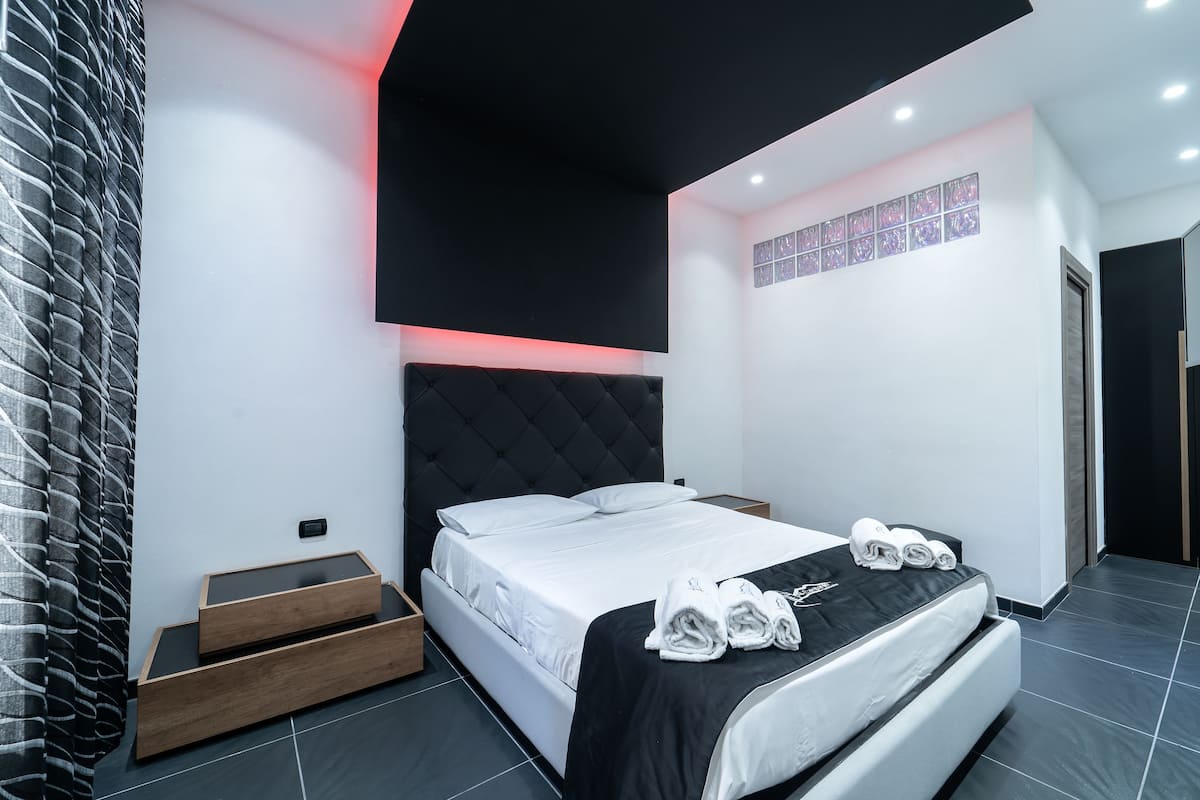 A modern bedroom with a black headboard, a bed with white linens, and a set of towels on the bed.