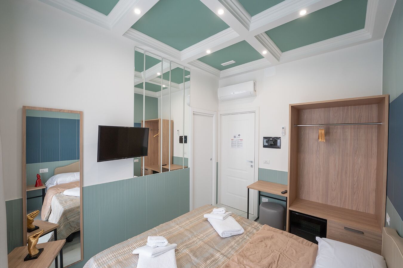 Habitació d'hotel amb llit, televisió, armari, mirall i taula petita.