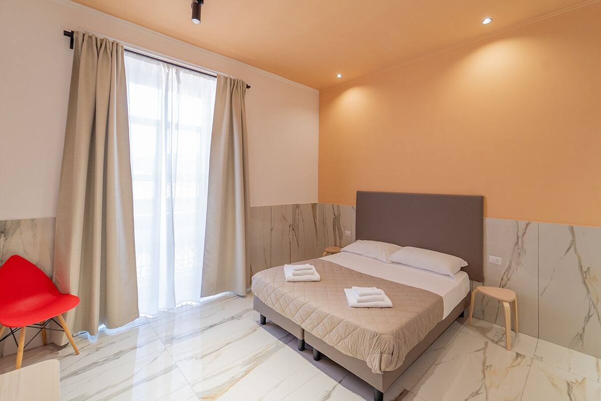 A hotel room with a bed, a red chair, and a window with curtains.
