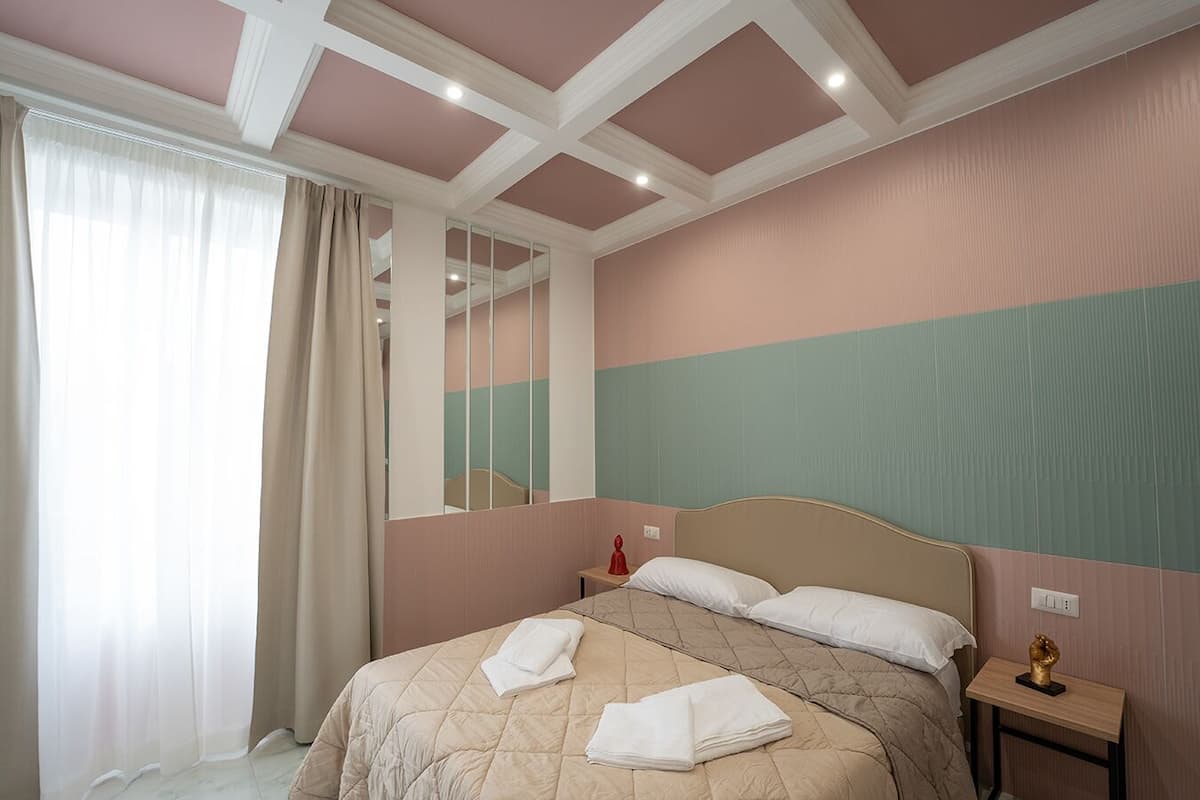 A bedroom with a bed, a nightstand, a mirror, and a window with curtains.