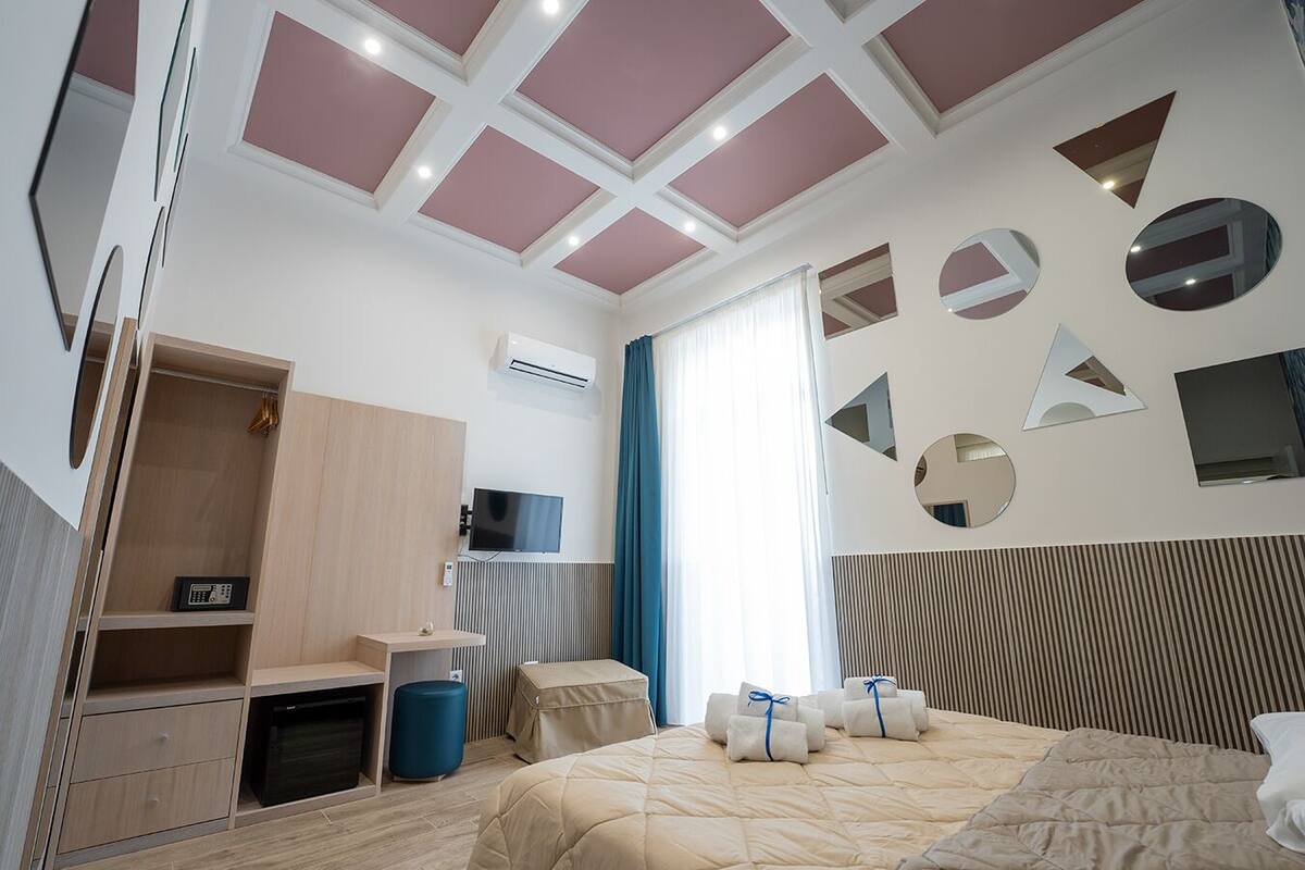 A modern hotel room with a bed, a desk, a wardrobe, and a television.
