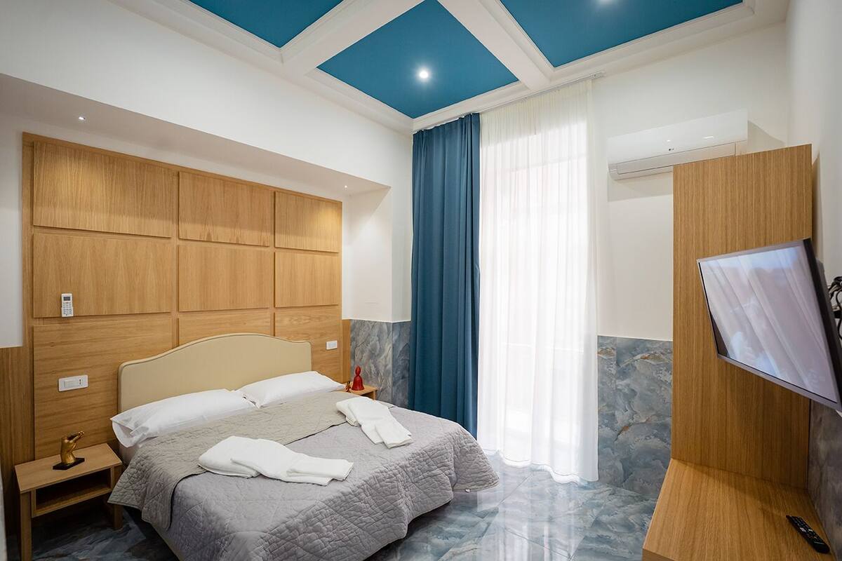 A hotel room with a bed, a nightstand, a TV, and a bathroom with a shower.
