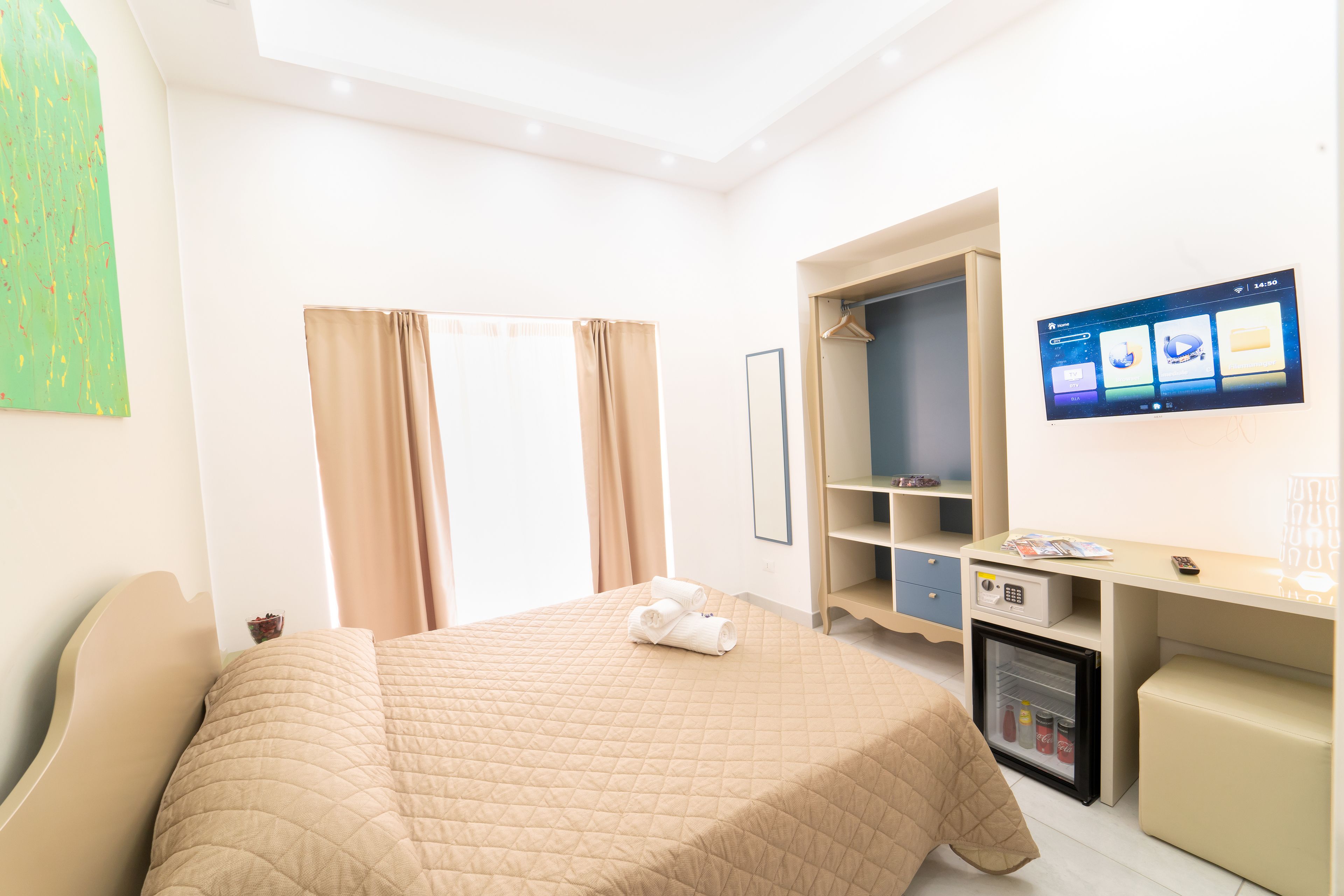 A hotel room with a bed, a desk, a mini-fridge, and a TV on the wall.