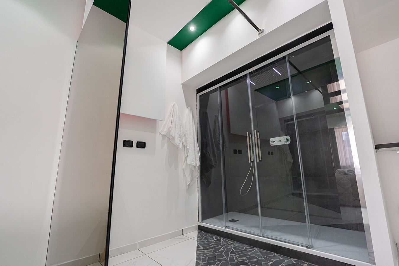 Une salle de bain moderne avec une douche à parois de verre, un carrelage blanc au sol et une touche de vert au plafond.
