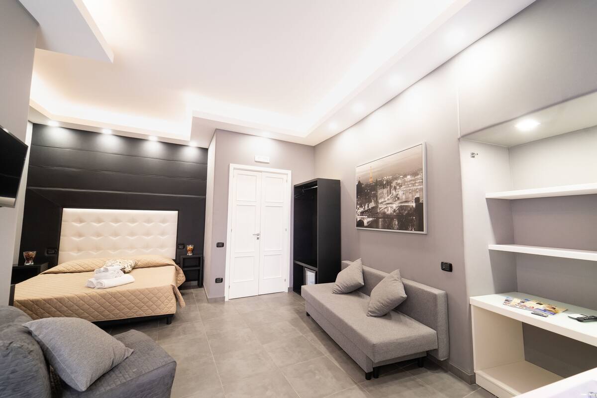 A modern bedroom with a bed, a sofa, a TV, and a bookshelf.