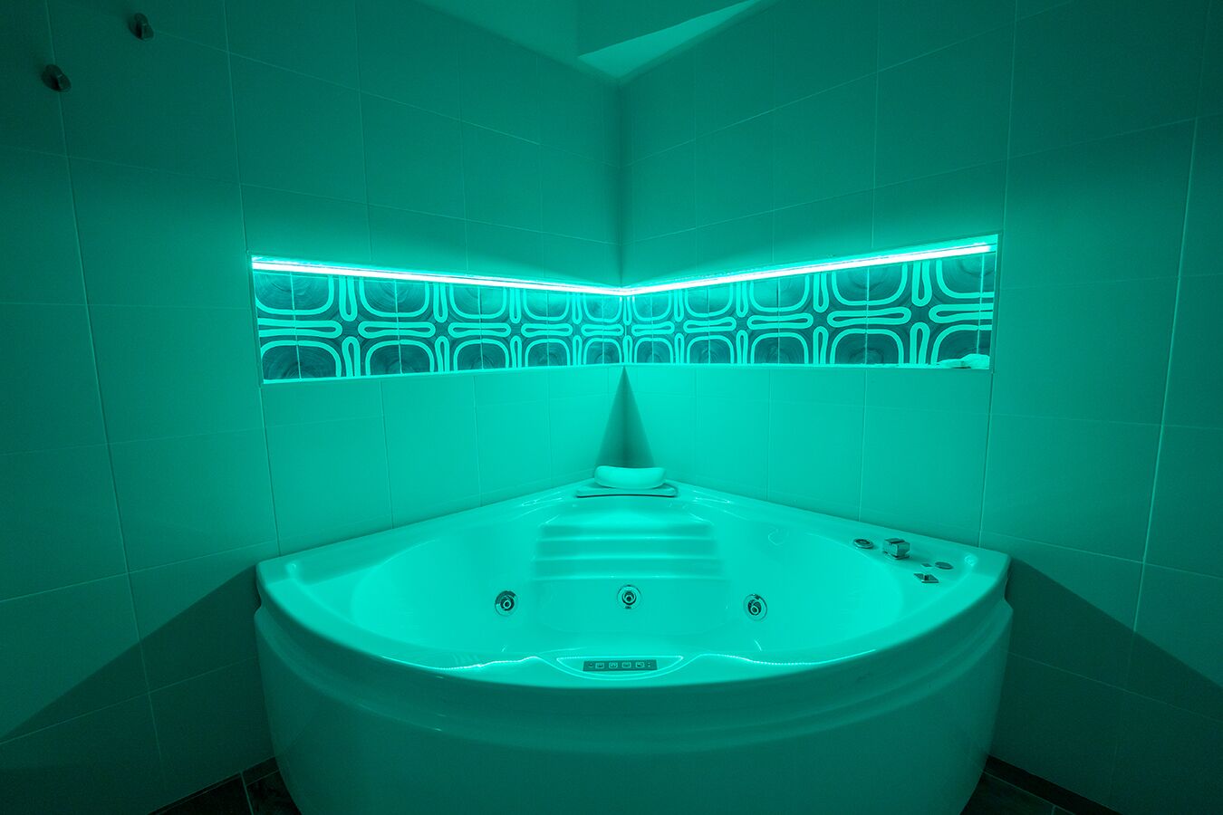 Ein modernes Badezimmer mit einer zentralen Whirlwanne, blaugrünem Licht und gemusterten Wandfliesen.