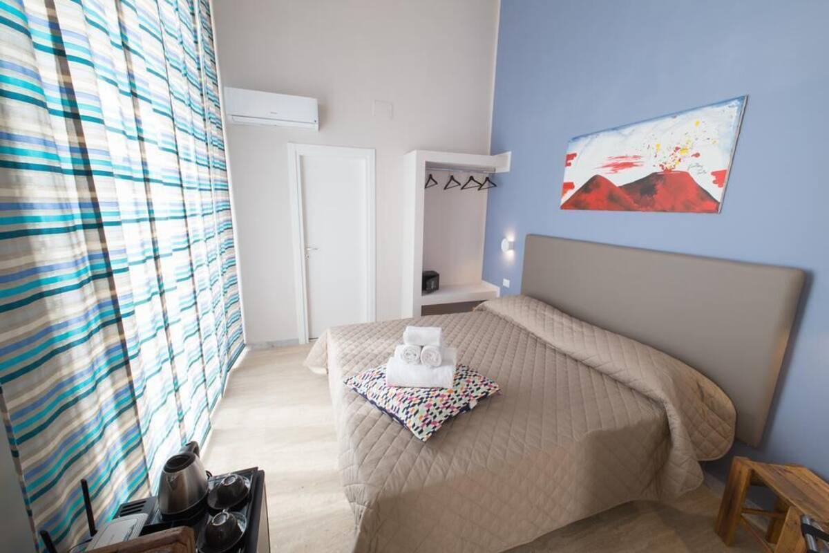 Ein Schlafzimmer mit einem Bett, einem Nachttisch, einem Sessel, einem Fenster mit Vorhängen und einem Bild an der Wand.
