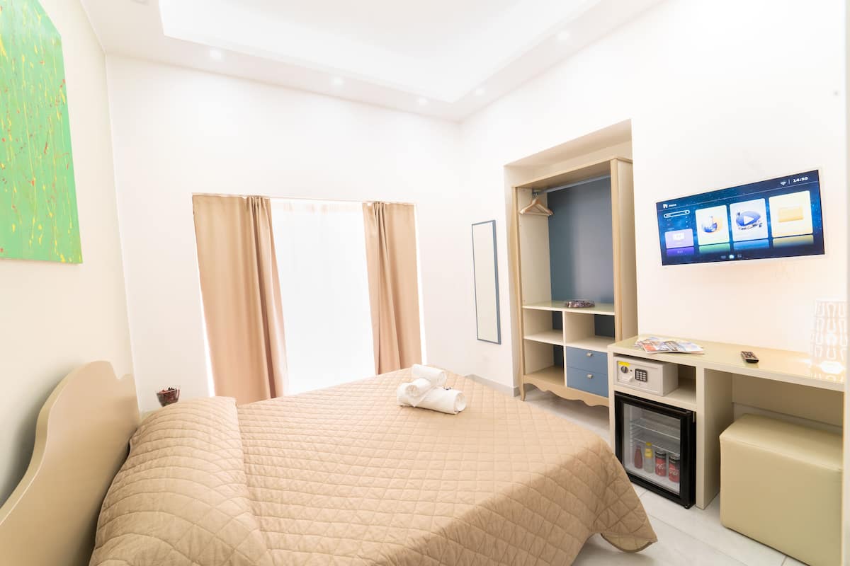 Ein Hotelzimmer mit Bett, Schreibtisch, einer Minikühlschrank und einem Fernseher an der Wand.