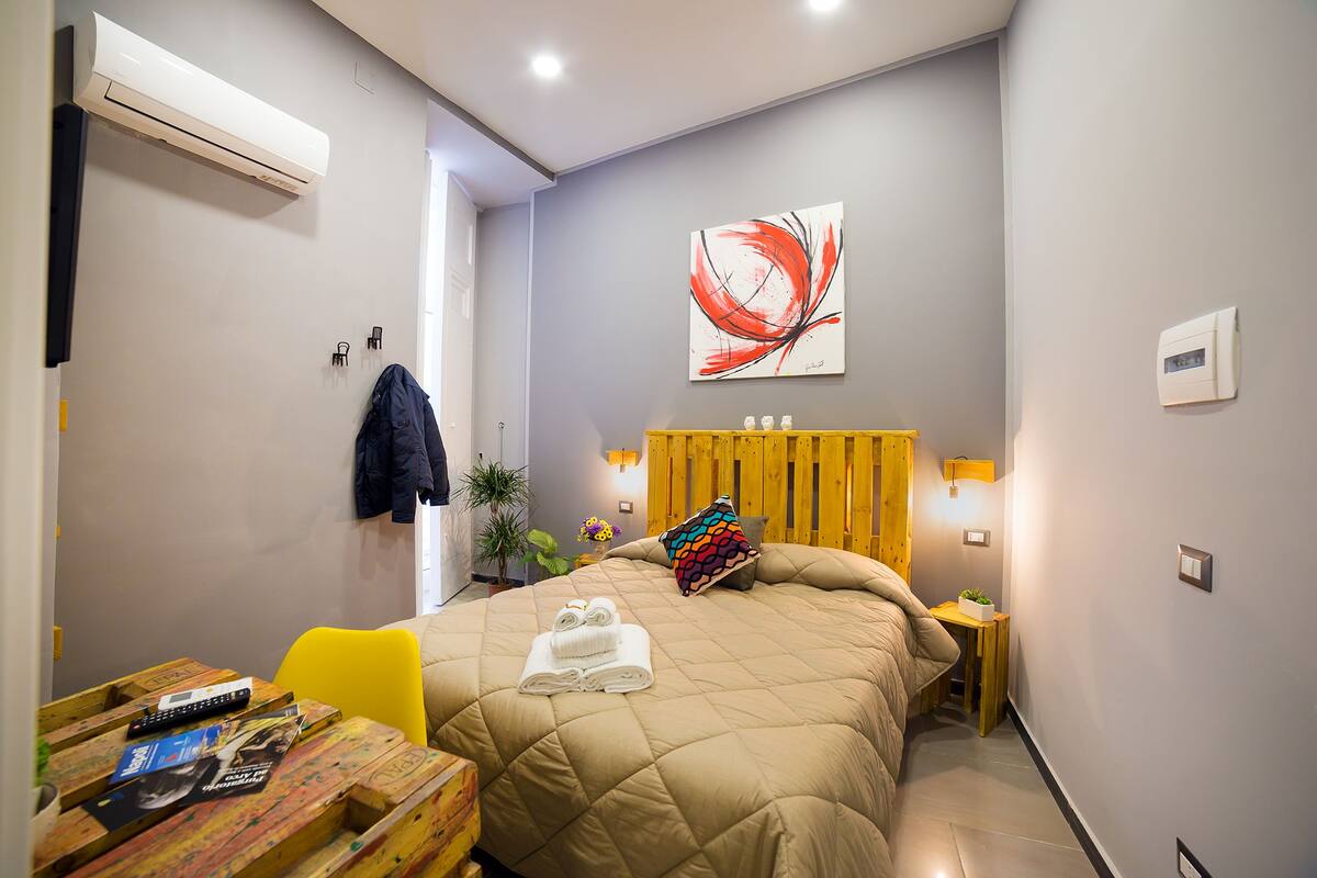 Ein Hotelzimmer mit einem Bett, einem Nachttisch mit Lampe, einer Wandklimaanlage und einem Gemälde.