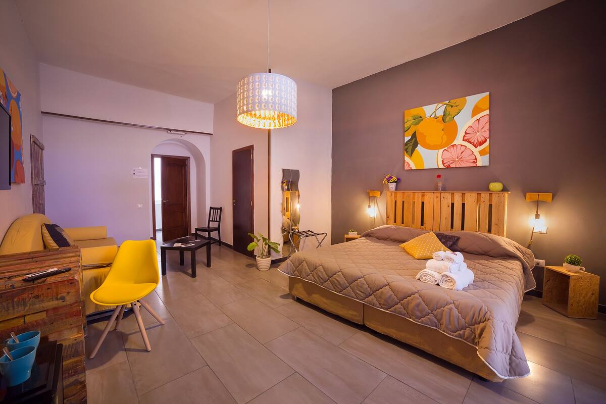 Ein modernes Schlafzimmer mit einem großen Bett, einem gelben Sessel, einem Schreibtisch und einem Essbereich.