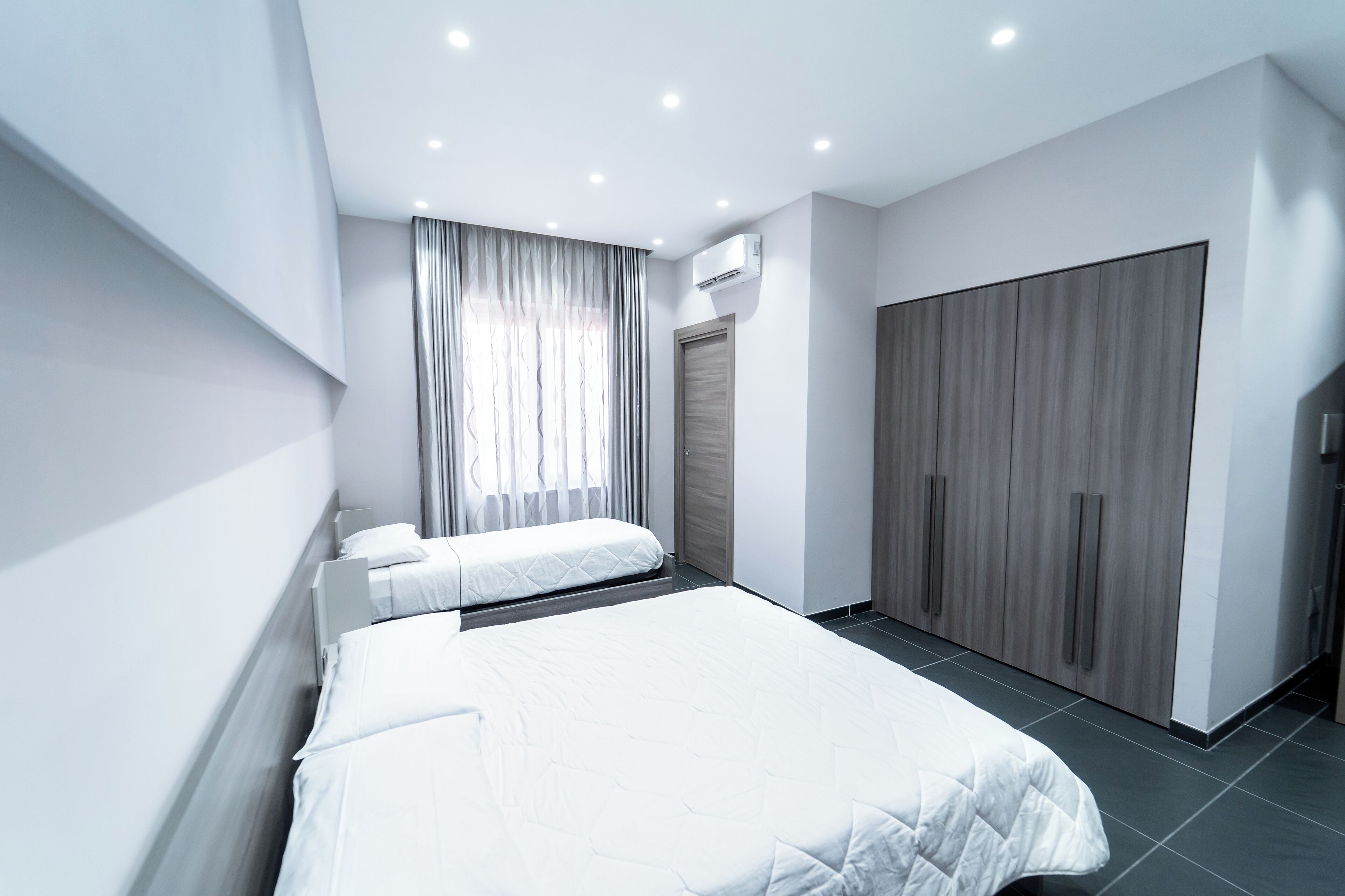 Una habitación de hotel moderna con una cama grande, una cama más pequeña, un armario y un equipo de aire acondicionado.
