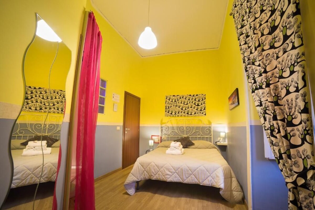 Habitación de hotel con dos camas, un espejo, una cortina roja y un papel tapiz estampado.