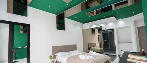 Habitación de hotel moderna con una cama grande, zona de ducha independiente y una mesa de comedor con libros y un cactus.