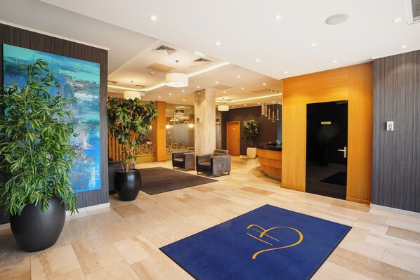 A modern hotel lobby with a reception desk, seating area, and large potted plants. - Hotel Briliant (Cluj-Napoca)