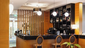 Zona de bar con sillas de madera, una barra y un estante con botellas.