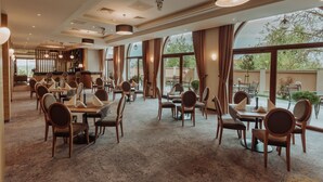 Un comedor amplio con múltiples mesas y sillas, ventanas grandes que ofrecen vistas al exterior y un diseño moderno de techo con iluminación empotrada.