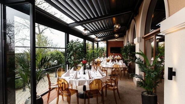 Un restaurante con mesas redondas, sillas y plantas en macetas.