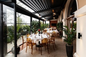 Un restaurante con mesas redondas, sillas y plantas en macetas.