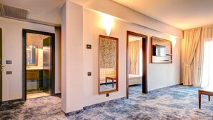 Habitación de hotel con piso de mármol, un espejo grande, sofá, televisor y ventana con cortinas.