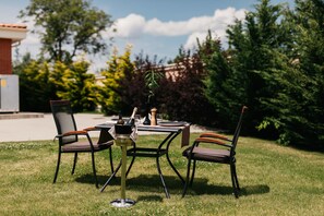An outdoor dining area with a table and chairs, surrounded by greenery and a building in the background. - Hotel Briliant (Cluj-Napoca)