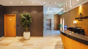 Zona de recepción de un hotel con un mostrador de madera, una planta en maceta, un mostrador de recepción y un letrero en la pared del hotel.