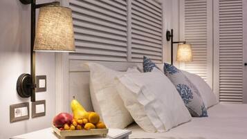 A bedroom with a bed, white bedding, a fruit bowl on a bedside table, and two wall-mounted lamps.