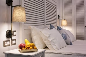 Ein Schlafzimmer mit einem Bett, weißer Bettwäsche, einer Obstschale auf einem Nachttisch und zwei Wandleuchten.