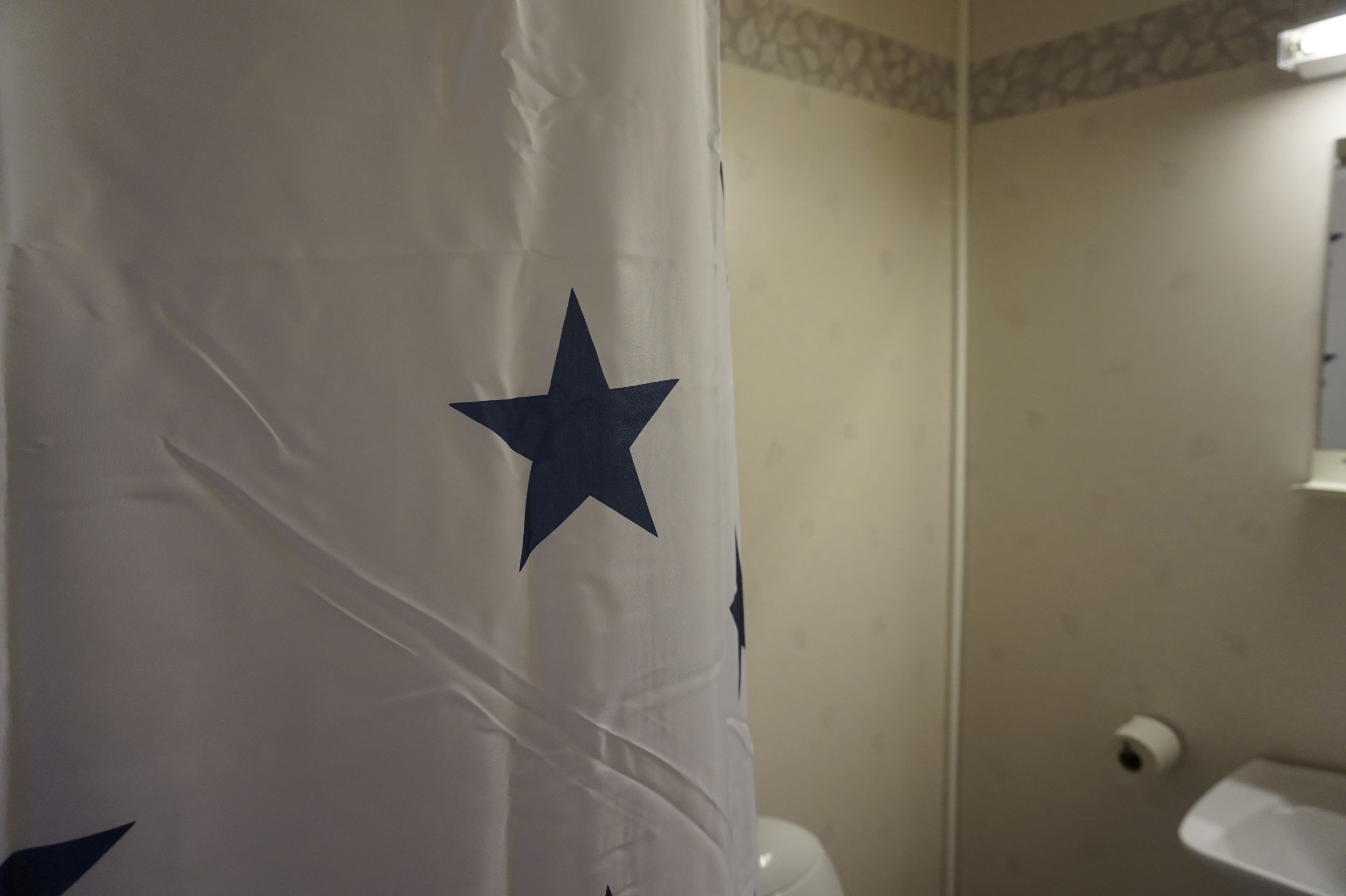A bathroom with a shower curtain featuring a large star design, a toilet, and a paper towel dispenser.