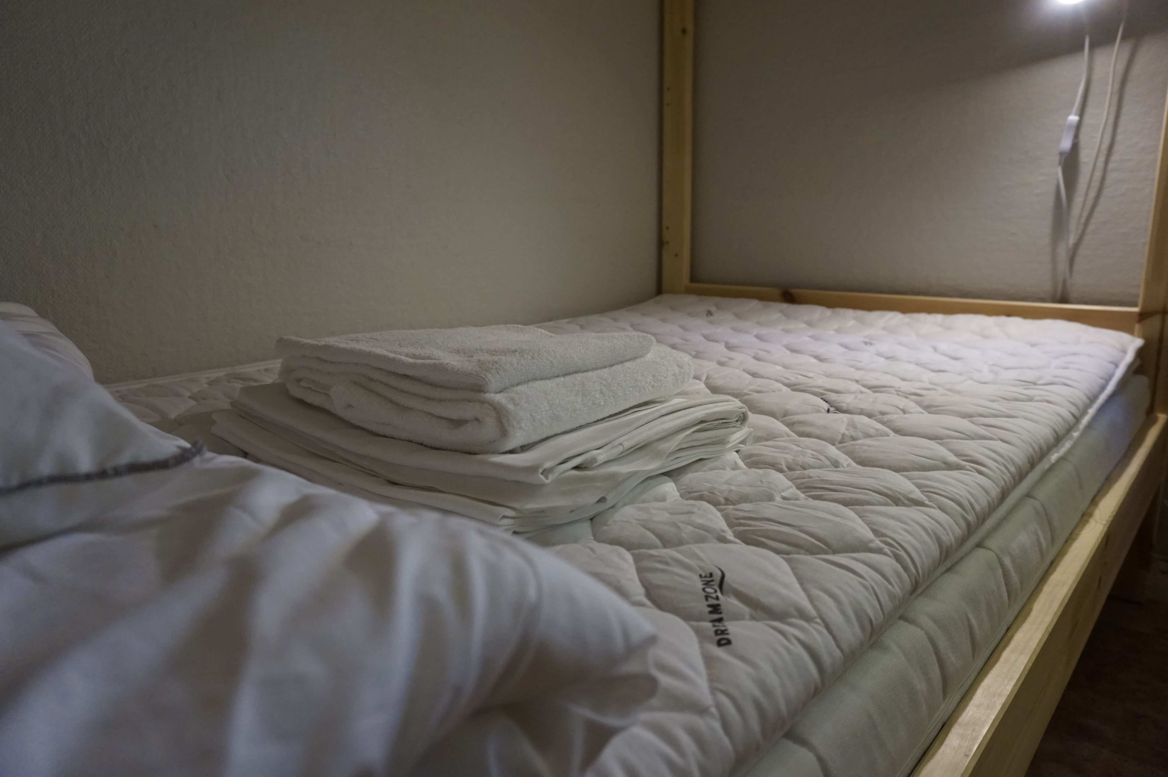 Un lit simple avec un matelas matelassé et des serviettes blanches soigneusement pliées, empilées sur le dessus.
