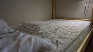 A single bed with a quilted mattress and neatly folded white towels stacked on top.