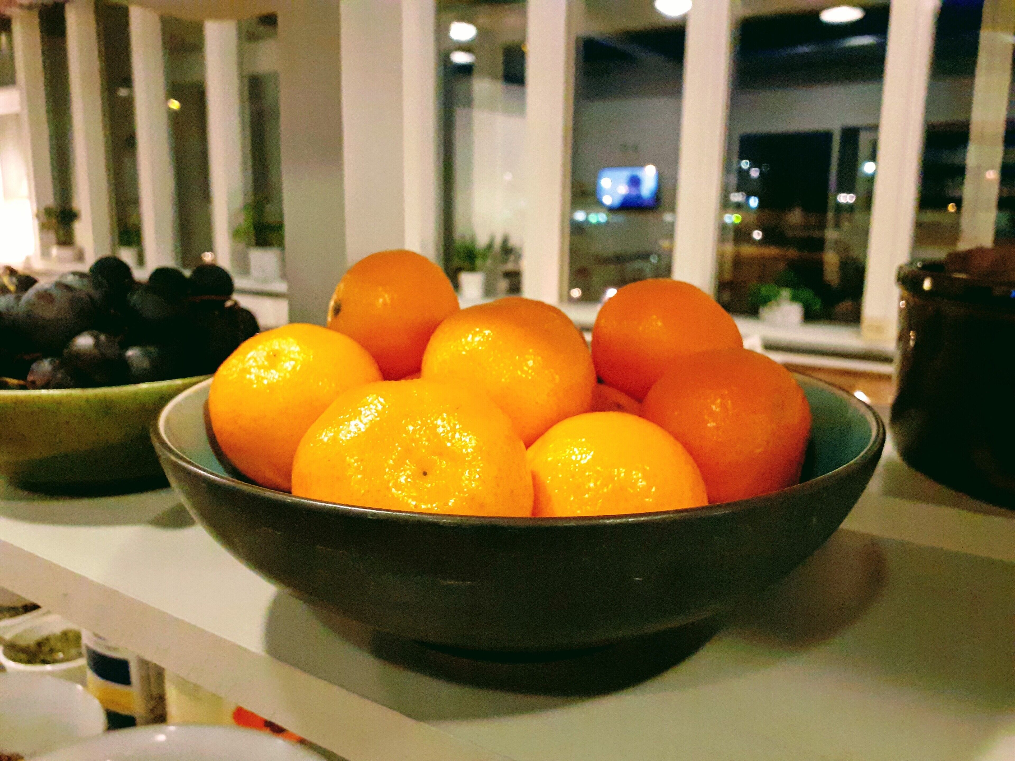 A bowl of oranges on a kitchen counter with a window in the background.