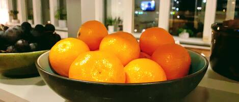 A bowl of oranges on a kitchen counter with a window in the background.