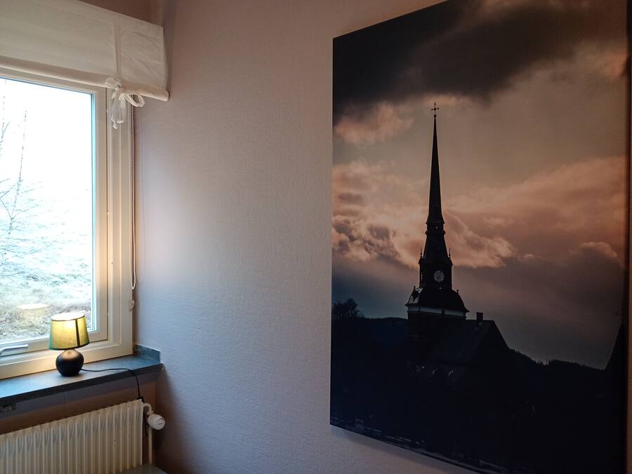A room with a window, a radiator, and a wall-mounted picture of a church spire.