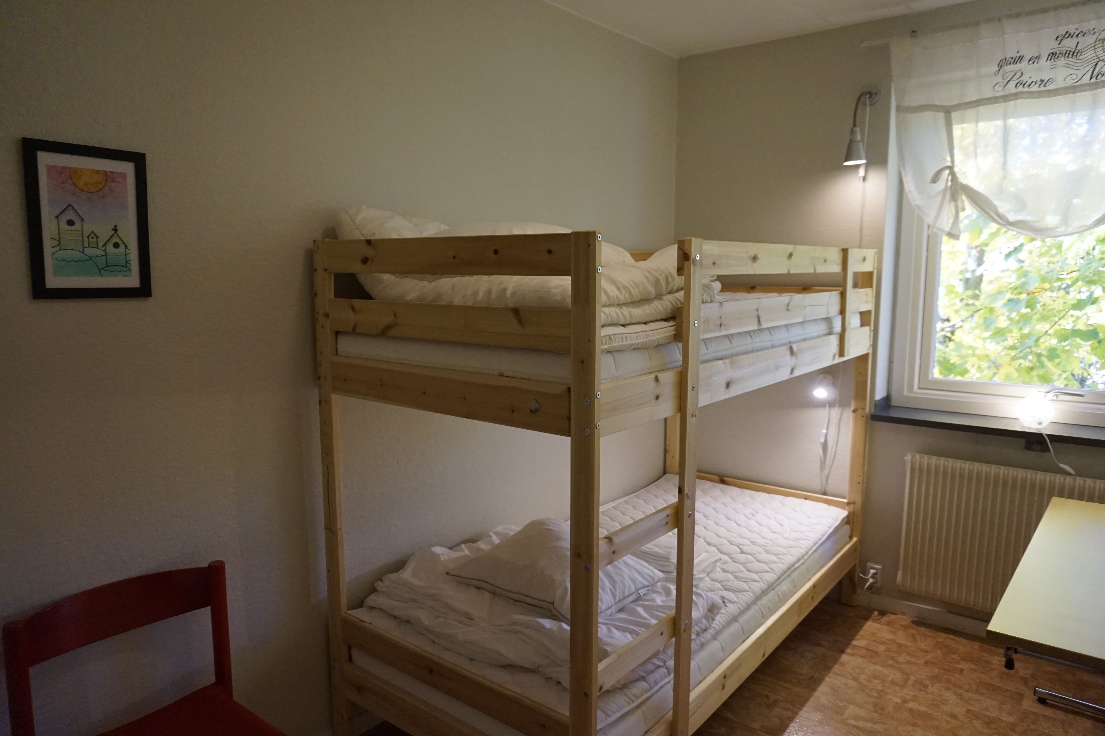 Habitación con literas, una ventana, un radiador y un cuadro en la pared.