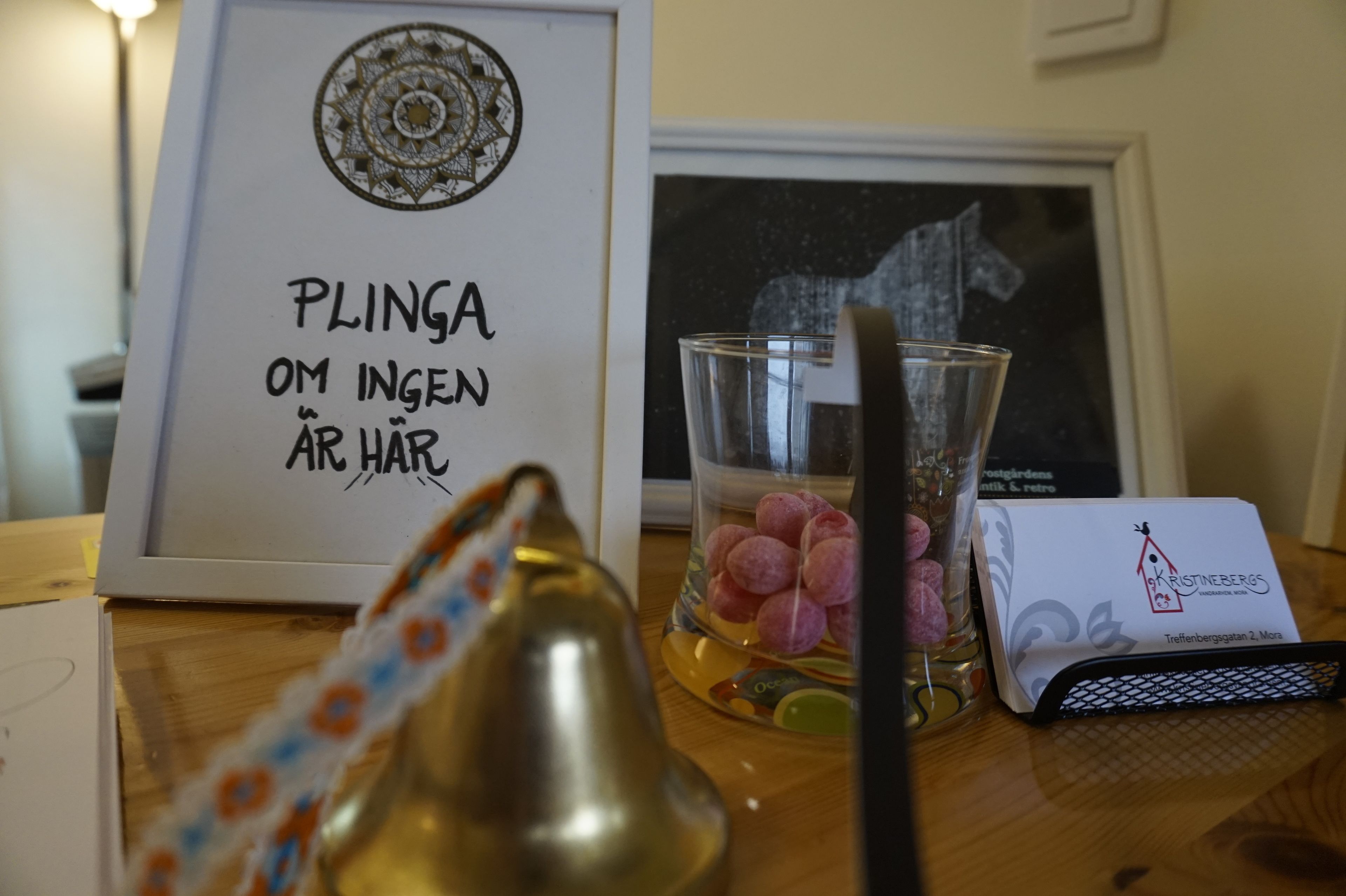 Une photo encadrée avec une inscription, un verre rempli de bonbons, une cloche et une carte de visite, le tout pos é sur une table en bois.