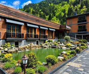 Ein Hotel mit Steinfassade, einem Teich und einer Bergkulisse.