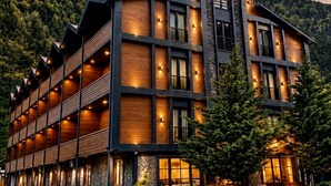 Un hôtel à plusieurs étages, doté d’un design moderne, avec une façade en pierre et des éléments décoratifs en bois, le tout se dressant sur un fond de paysage montagneux.