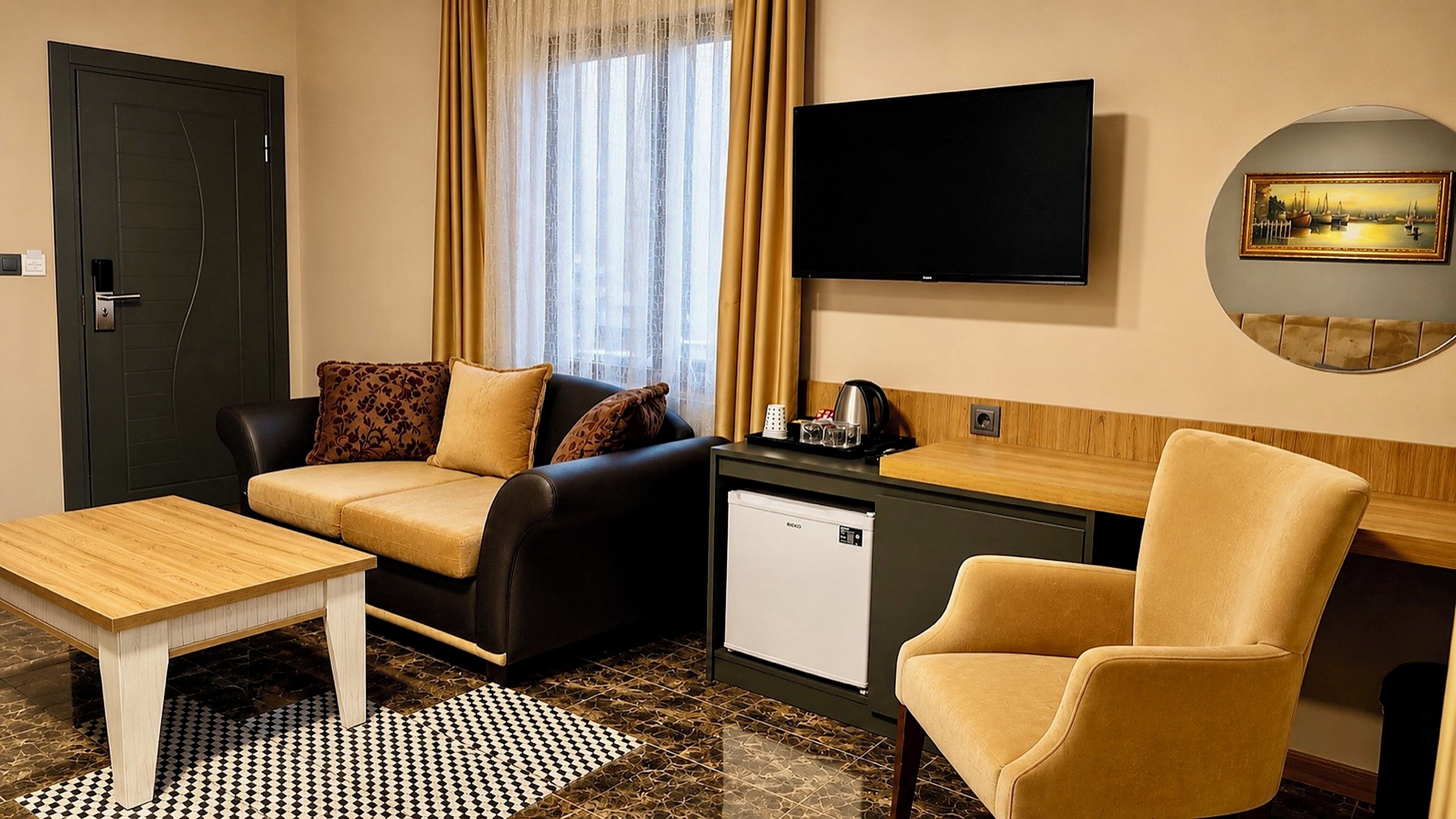 A hotel room with a sofa, a desk, a chair, a television, and a small refrigerator.