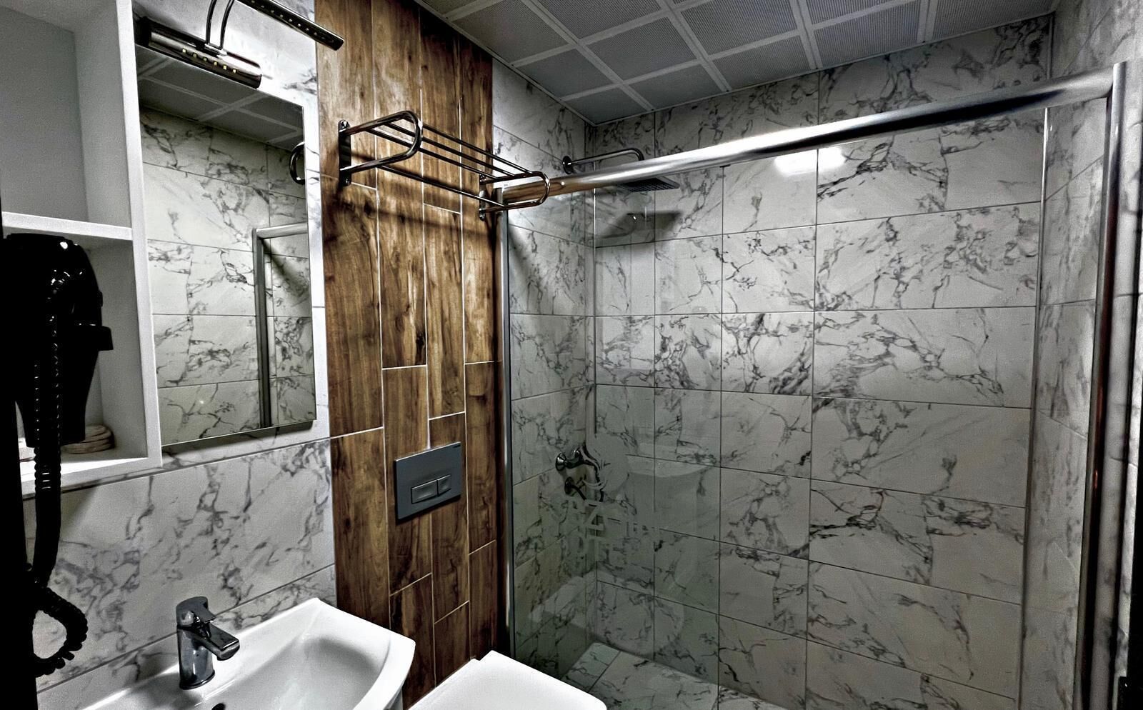 Une salle de bain avec un meuble-lavabo en bois, un évier, un miroir et une douche dotée d’une porte en verre.