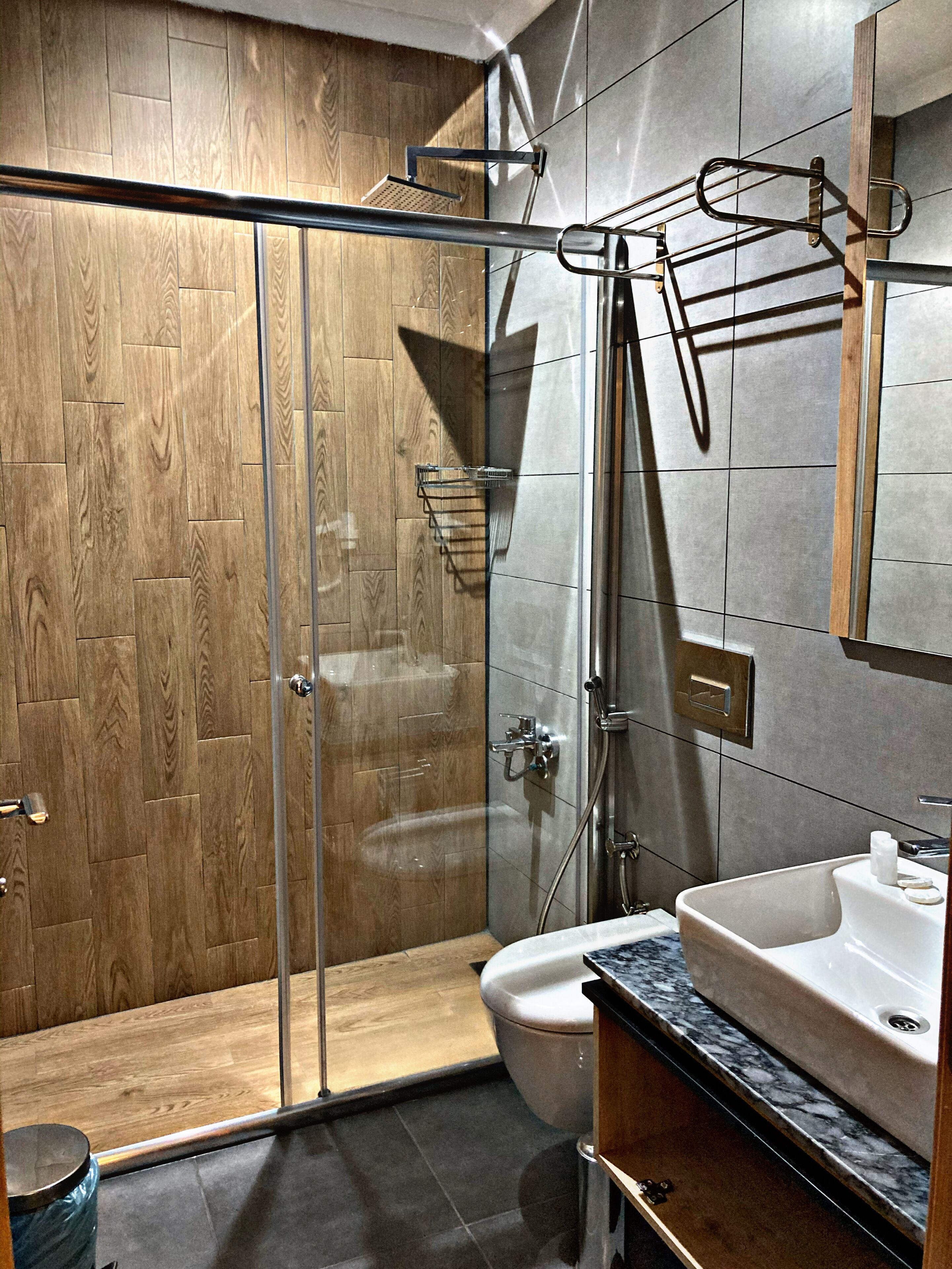 Un baño moderno con cabina de ducha de vidrio, tocador de madera y encimera de mármol.