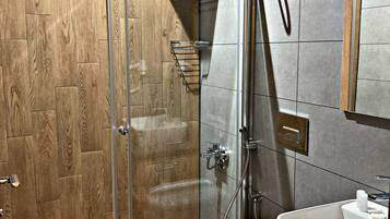 Un baño moderno con cabina de ducha de vidrio, tocador de madera y encimera de mármol.